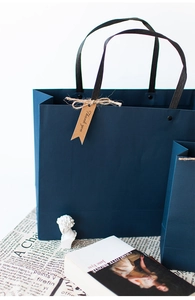 Detail of navy blue gift bag with black woven handle and Thank You kraft paper tag