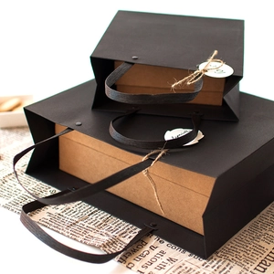 Minimalist black paper gift bag with rivet handles and kraft inner box on vintage background
