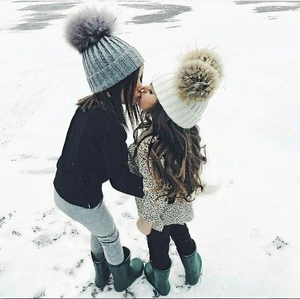 Winter kids knit hats with large pom poms shown in outdoor snowy lifestyle setting