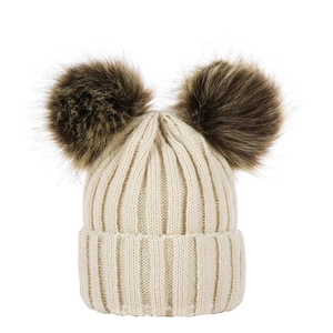 Detail view of beige knitted baby hat featuring two large fluffy faux fur pompoms