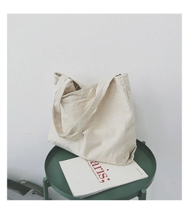 Minimalist beige canvas tote bag displayed on a green side table with a magazine backdrop