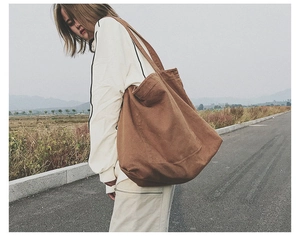 Lifestyle shot of a brown oversized canvas tote bag worn by a model on a scenic road