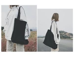 Detailed view of a black large capacity canvas tote bag worn by a model in outdoor setting