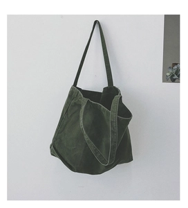 Detail of green canvas tote bag shoulder strap and texture hanging on a white wall