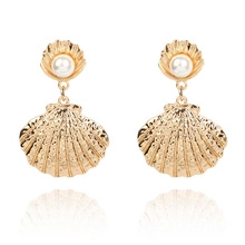 Détail macro de boucles d'oreilles coquillage doré avec perles blanches au centre