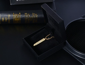 Macro detail of golden cross bullet pendant urn for ashes placed in a black velvet gift box