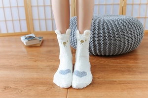 Close-up of white plush bear socks with grey heart patterns on warm wooden floor