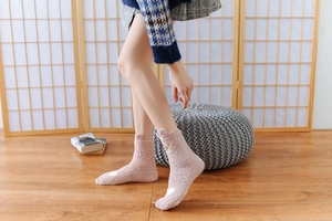 Close-up of pink coral fleece socks with white heart patterns on cozy wooden floor