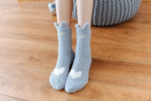Close-up of grey coral fleece socks with white heart and animal ear details on wood floor