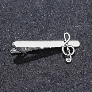 Close-up of a silver musical note tie clip on a textured black surface for business shirts