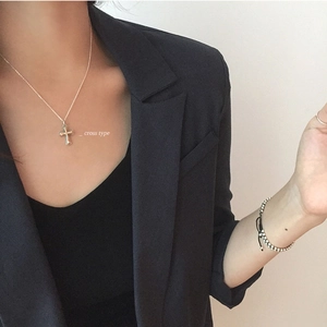 Detail of a minimalist gold cross pendant necklace on a model with subtle bead bracelet