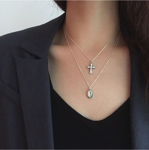 Close-up of layered S925 silver necklaces with cross and oval vintage pendants on neck
