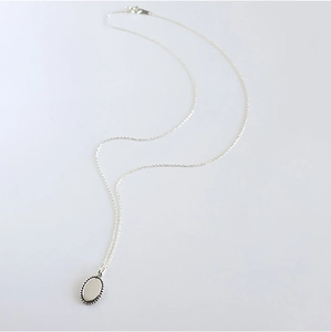 Detail shot of a polished silver oval pendant necklace with a beaded edge on white background