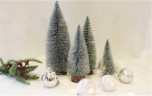 Close-up of four mini flocked Christmas trees with natural wood bases in a snowy scene