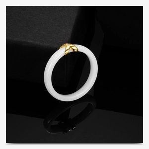 Close-up of white ceramic ring with gold X detail and diamond on black background