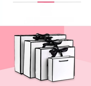 Stack of white premium paper gift bags with black border design and ribbon handles