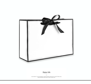Detail of minimalist white gift bag with black edges, ribbon bow, and artistic text