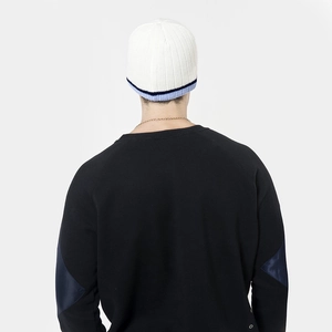Detail view of white knitted beanie with navy blue stripes and patchwork sleeve sweater