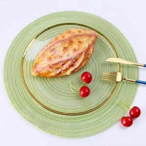 Detail of round glass dinner plate with gold rim and green woven heat resistant placemat