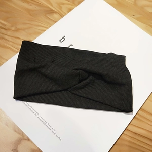 Close-up of black knitted twist headband showing fine texture and cross-knot design