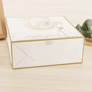 Detail of white paper gift bag with golden rose print and beige cotton rope handles