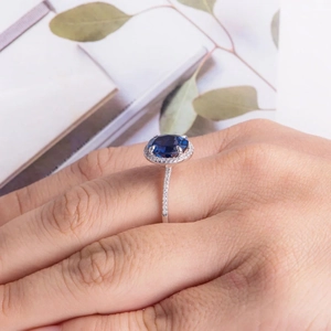 Elegant model wearing a halo set silver ring with an oval royal blue gemstone centerpiece