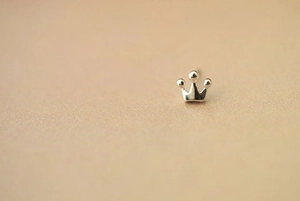 Macro shot of minimalist silver crown stud earring on a warm beige background