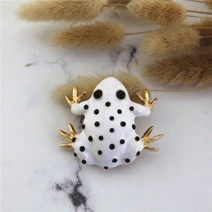 Detailed macro view of white enamel frog brooch with gold finish on marble surface
