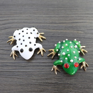 Detailed macro view of white and green enamel frog brooches with pearls and red crystals