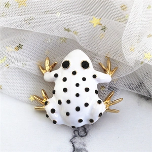 Detailed macro view of an enamel frog brooch with white glaze and gold plating finish