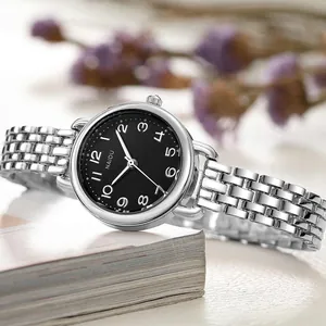 Close-up of a silver quartz watch with a black dial on a book with blurred lavender flowers