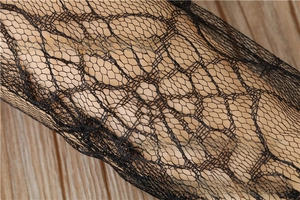 Close-up of black spiderweb lace fabric with floral patterns on a wooden surface