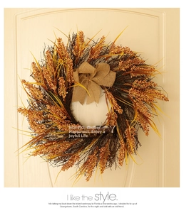 Close-up of harvest wreath with golden wheat and burlap bow on a white wooden door