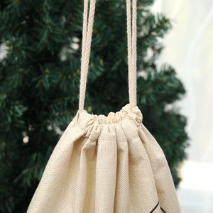 Close-up of beige burlap Christmas drawstring gift bag with rustic linen texture