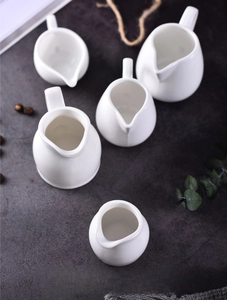 Macro shot of white ceramic creamer set with handles on dark stone background