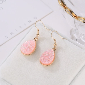 Elegant pink druzy teardrop hook earrings with gold-plated finish on a velvet jewelry tray