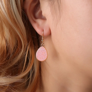 Detailed close-up of a pink glitter waterdrop earring with a gold-tone hook on a model
