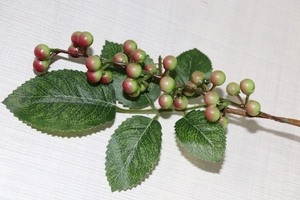 Detail of artificial berry branch with green to red gradient berries and textured green leaves