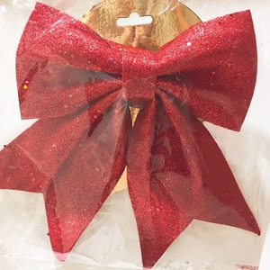 Detail of red glitter Christmas bow ornament showing shiny texture in protective packaging