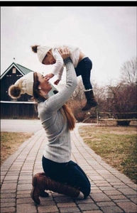 Matching mother and child wearing cream cable knit hats with faux fur pom poms outdoors