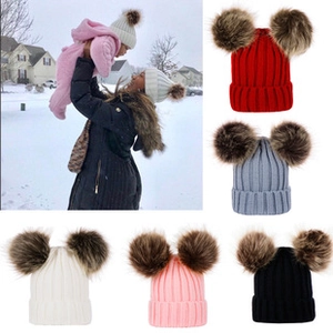 Detail view of colorful knitted baby beanies with double faux fur pom-poms for winter