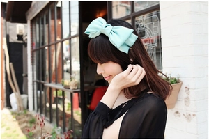 Detail shot of a mint green oversized layered satin bow headband on a model
