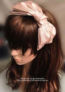 Detailed view of a large pink satin double-layered bow headband on wavy brown hair