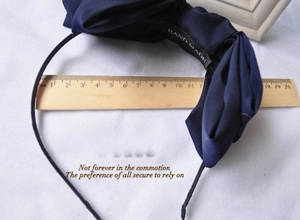 Detail showing oversized navy satin bow headband width measured with a wooden ruler