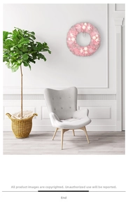 Pink Christmas wreath with white snowballs and stars hanging on a white wall above a sofa