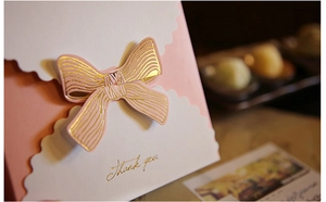 Détail de carte cadeau rose avec nœud, bords ondulés et inscription thank you dorée
