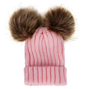 Detail of pink knitted baby hat with two large brown faux fur pom-poms for winter warmth