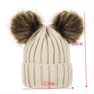 Detailed knit pattern and size measurements of a white baby beanie with faux fur pom poms