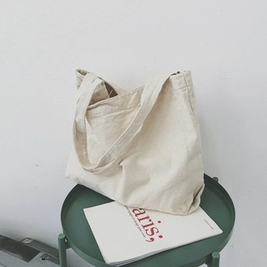 Minimalist cream white canvas tote bag displayed on a green table with a modern aesthetic