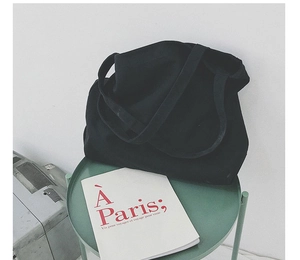 Minimalist black fabric tote bag placed on a green table with a vintage book backdrop